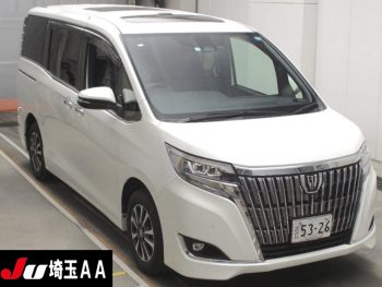 A luxurious 2019 Toyota Esquire Gi minivan in pristine white is parked indoors. The vehicle features a sleek and modern design, with a prominent chrome grille and sharp, sophisticated headlights. The minivan's clean lines and spacious body are accentuated by large windows and stylish alloy wheels, giving it an elegant and upscale appearance. The license plate and a small "JU" logo are visible, indicating it is from a Japanese auction.